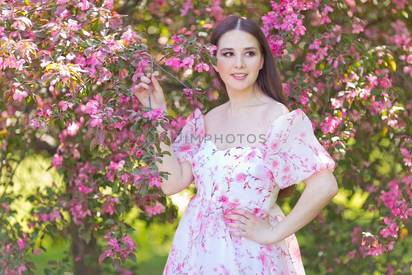Adorable smiling girl in dress, standing near a pink blooming by Zakharova