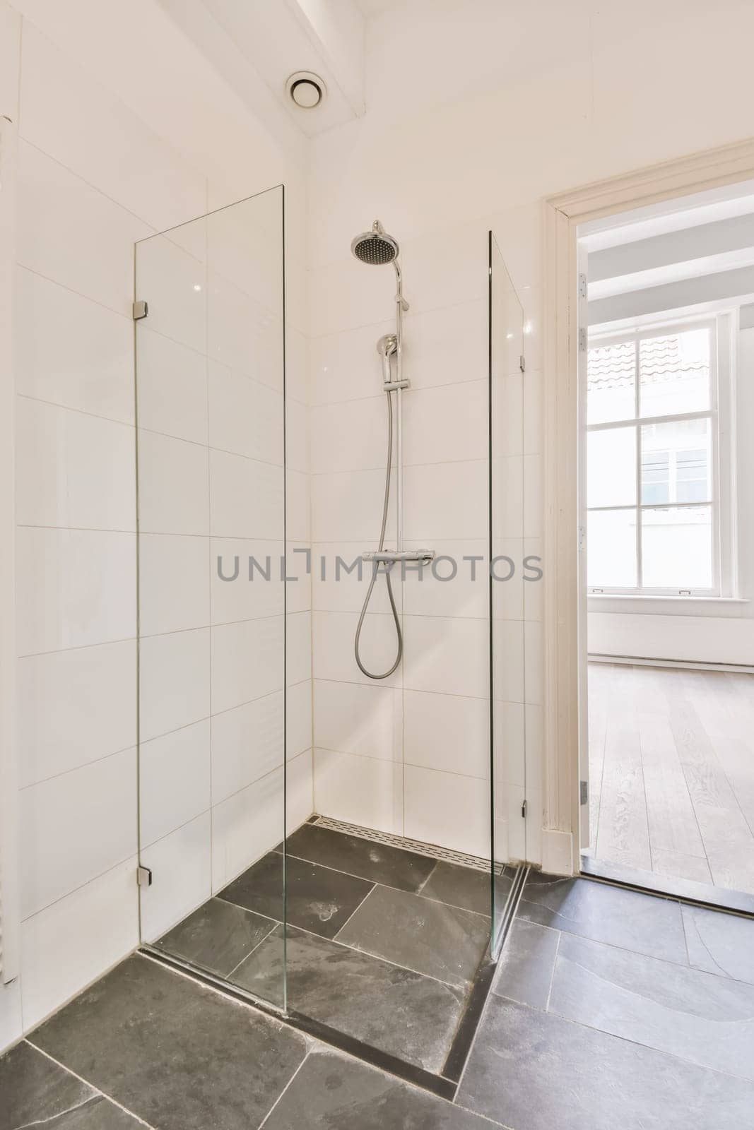 a white bathroom with black tile flooring and shower stall in the corner, there is a large window on the wall