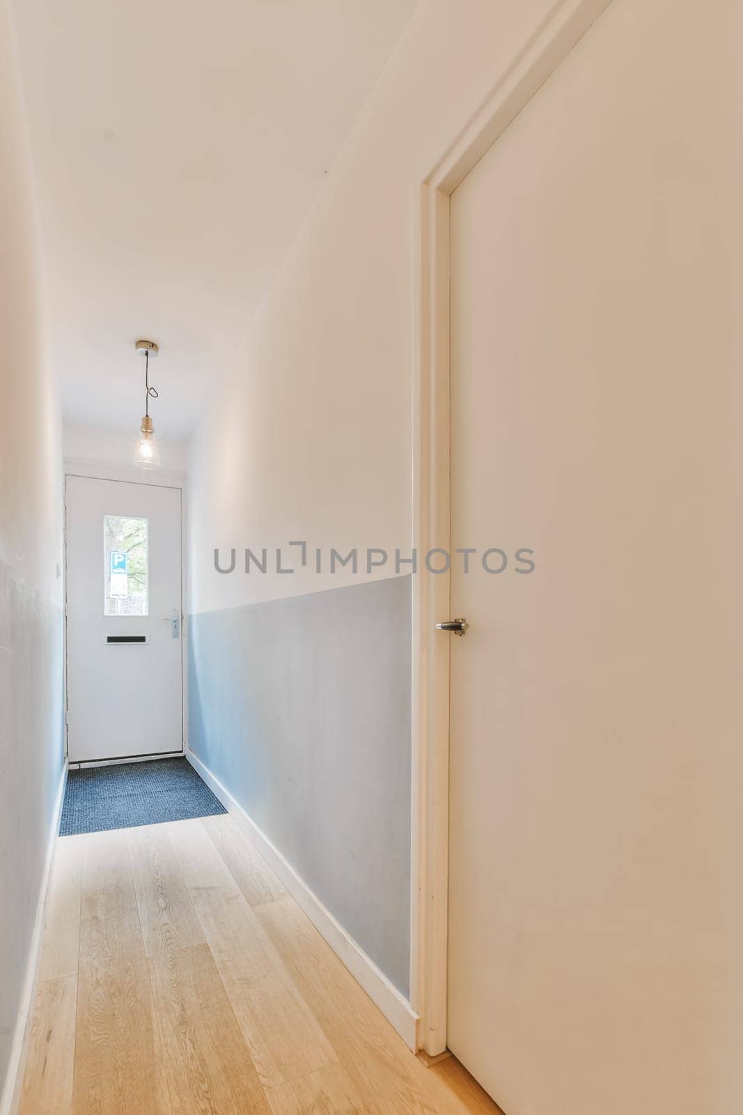 an empty hallway with wood floors and white walls, the door is open to reveal a light blue area in the room