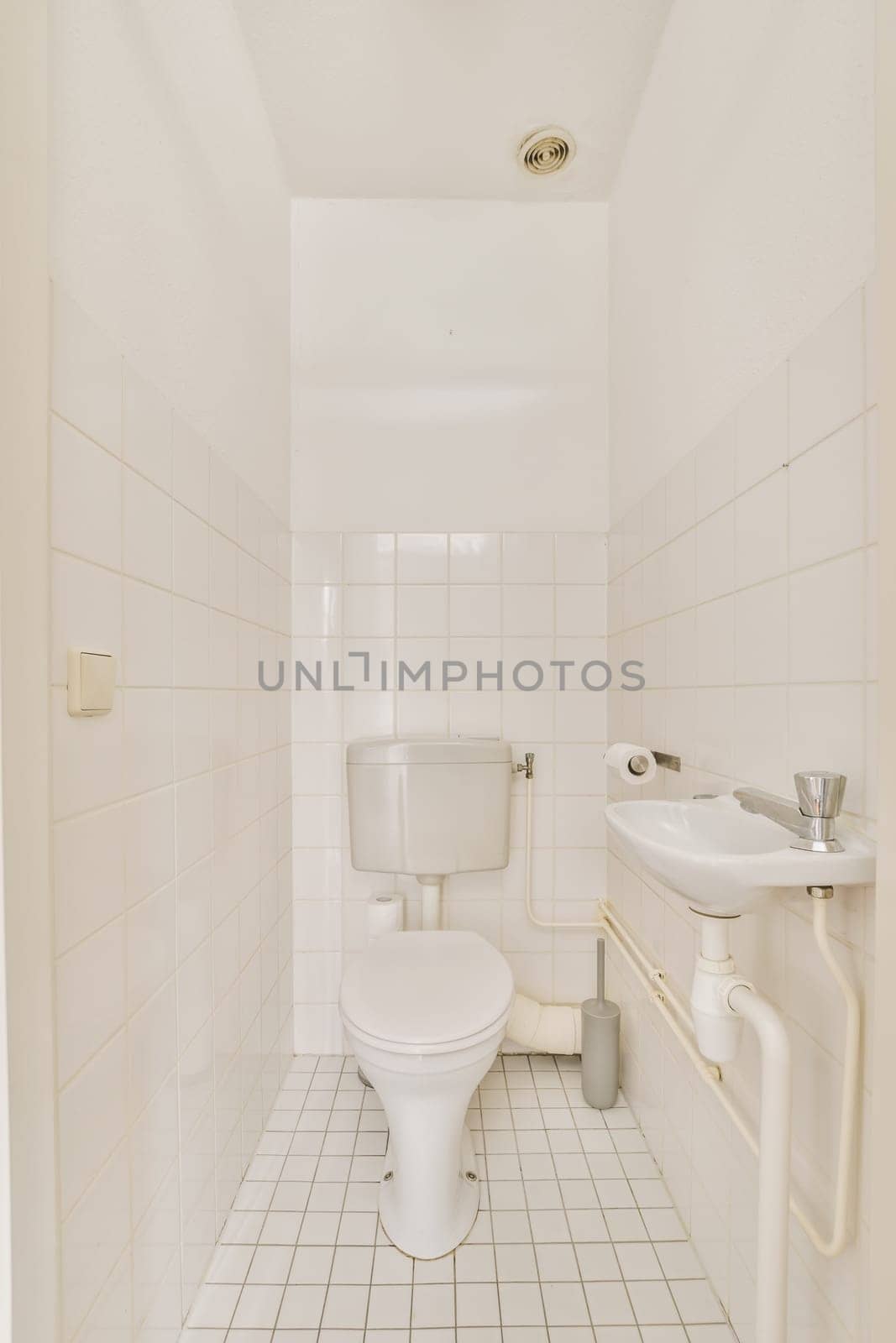 a bathroom with white tiles on the walls and floor, including a toilet in the middle part of the room