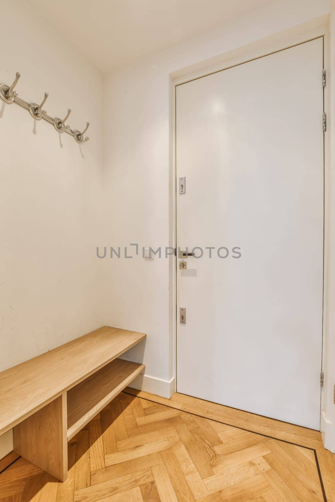 an empty room with wood flooring and white door leading to the entrance way in this apartment building, there is a bench on