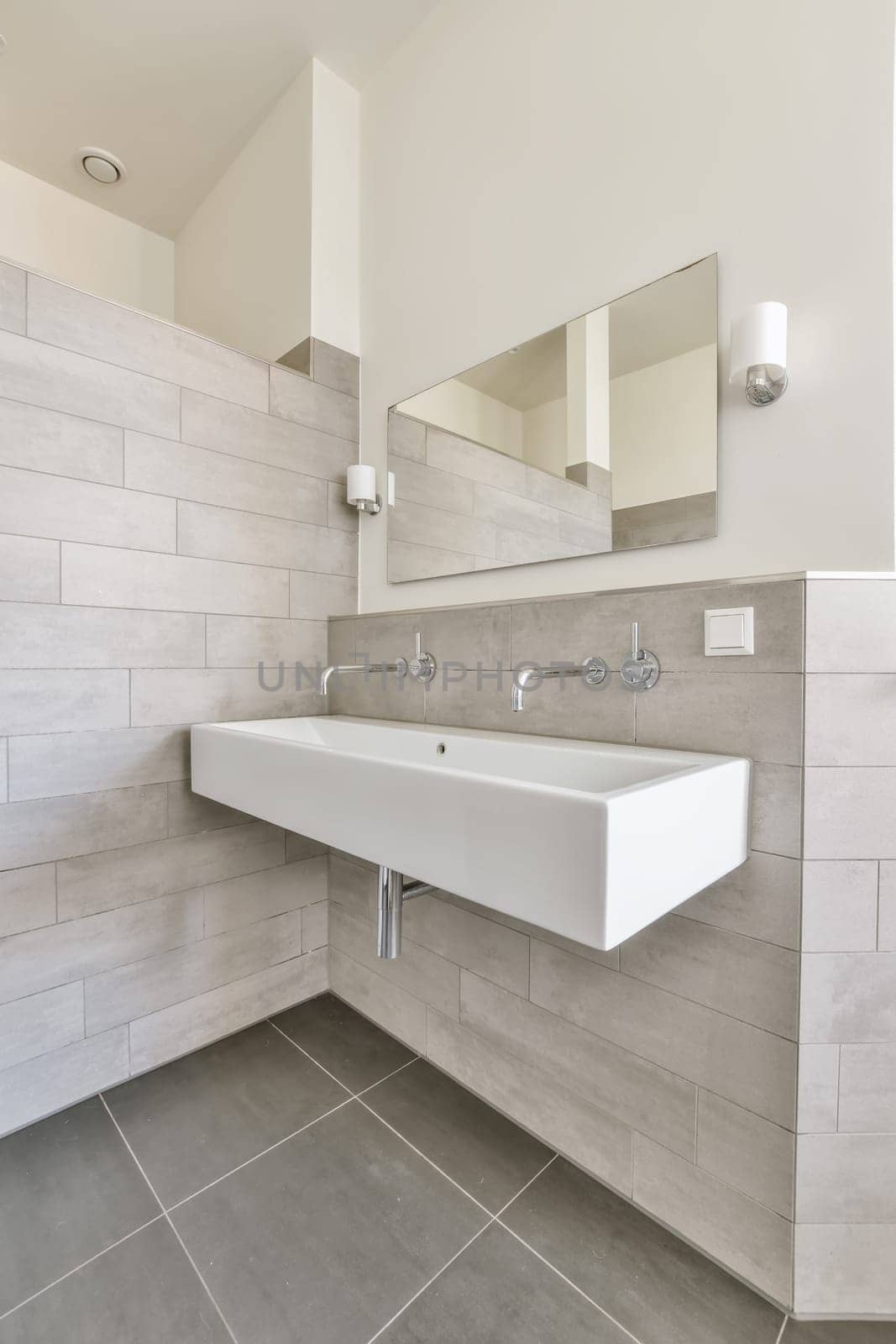 a modern bathroom with grey tiles and white fixtures on the wall above the sink is a large mirror in the corner