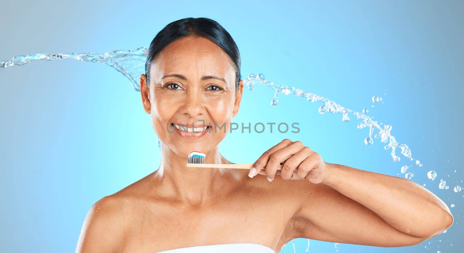 Dental, health and woman brushing teeth with toothbrush, toothpaste and water splash on blue studio background. Healthcare, self care product and oral care hygiene of mature Brazilian beauty model