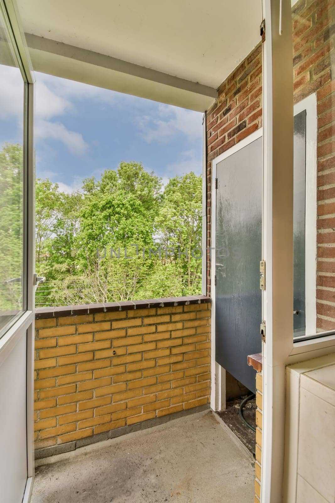 an empty balcony with brick wall and door leading out to the trees in the distance photo taken from inside outside