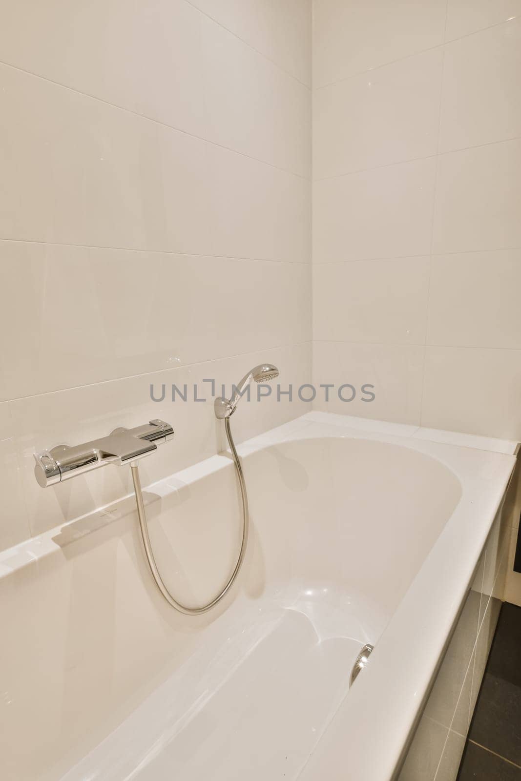 a white bathtub in the corner of a bathroom with black tiles on the walls and flooring around it