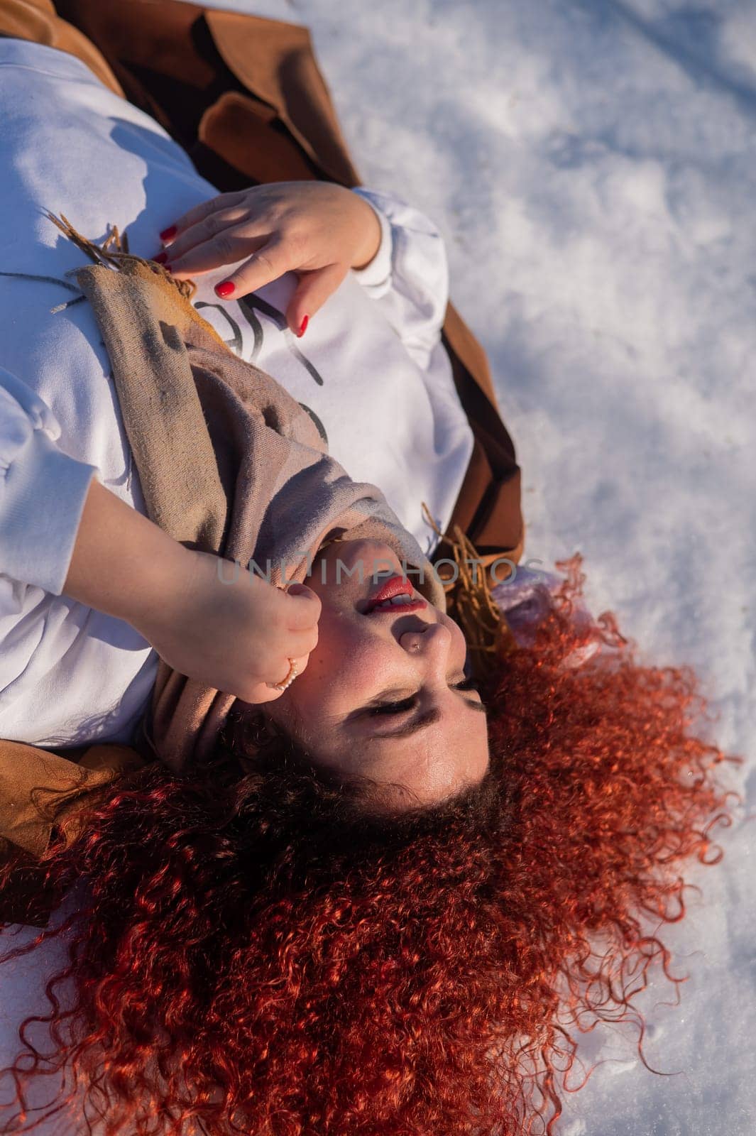 Top view of a fat red-haired woman lying on the snow