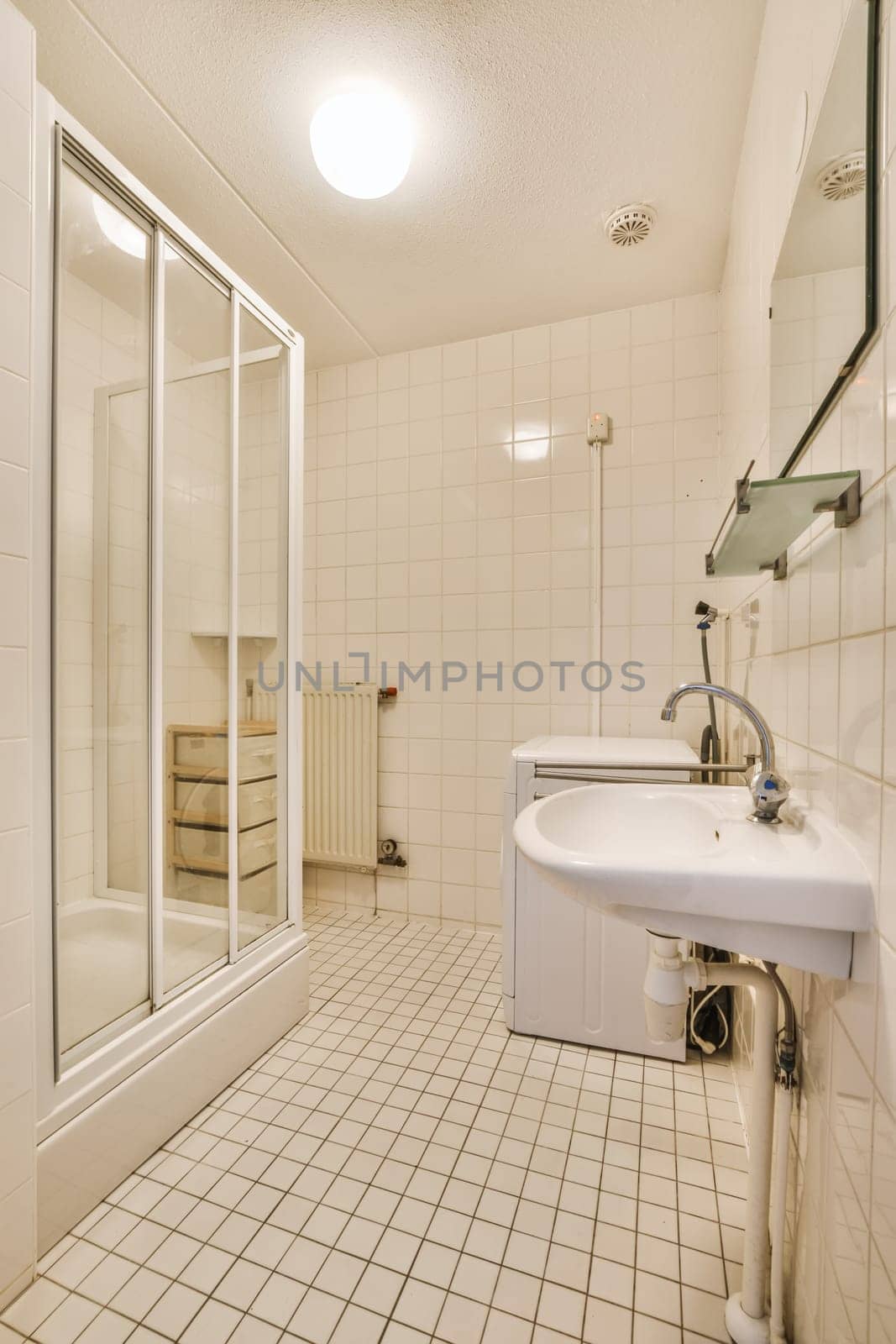 a bathroom with a sink, mirror and shower stall in the corner on the left is a white tiled floor