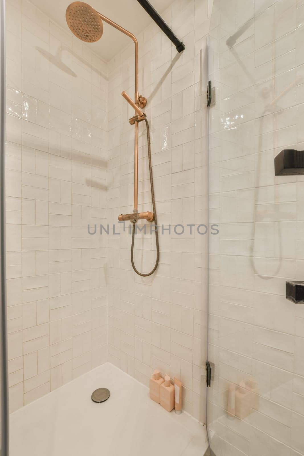 a white tiled shower with a gold shower head by casamedia