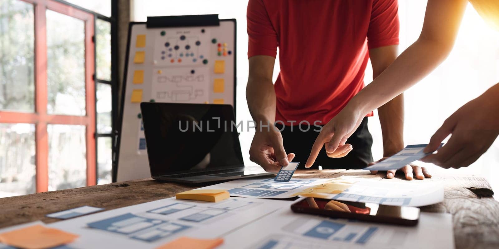 Close up ux developer and ui designer brainstorming about mobile app interface wireframe design at modern office. Creative digital development agency by nateemee