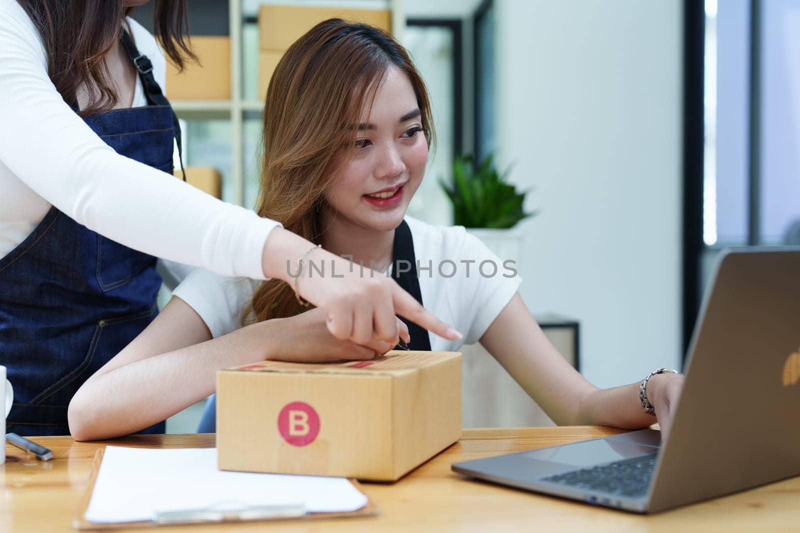 Starting small business two entrepreneur of independent Asian woman smiling using computer laptop with cheerful success of online marketing package box items and SME delivery concept by Manastrong