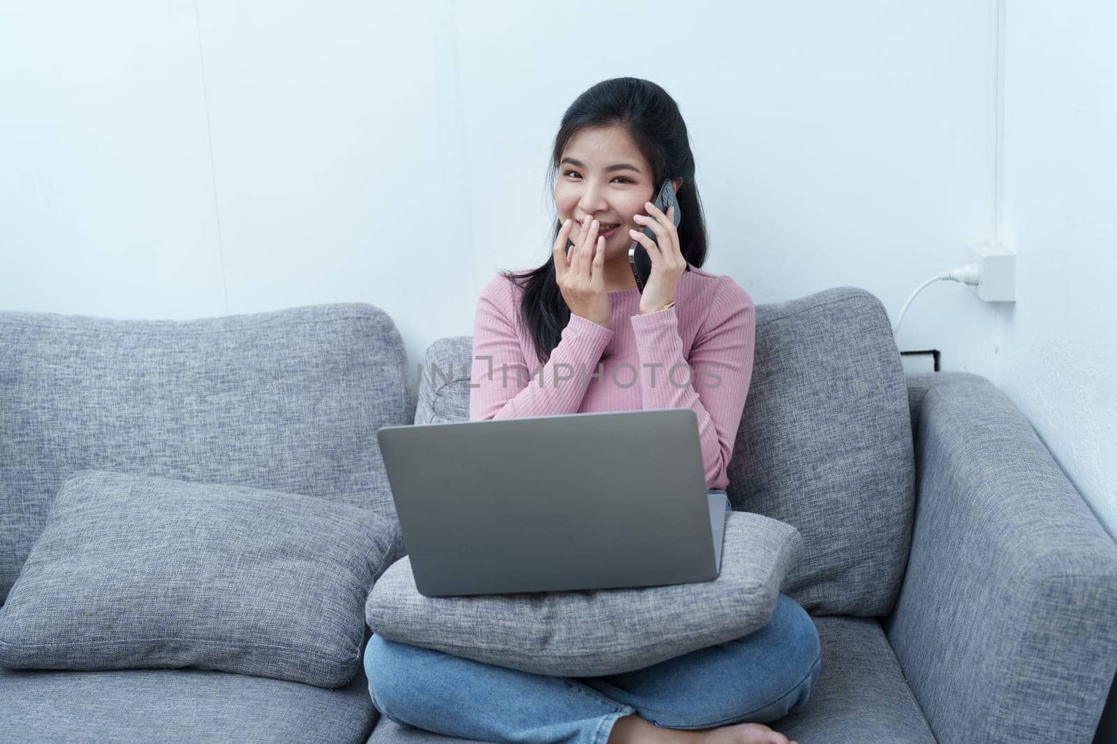 Portrait of a beautiful Asian teenage girl using her phone and computer sitting on the sofa at home by Manastrong