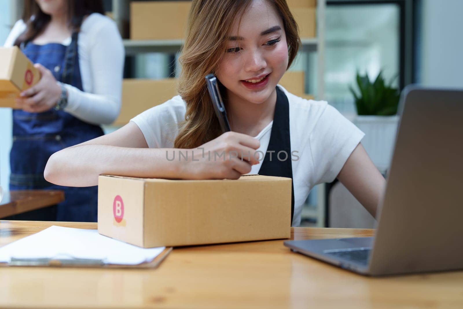 Starting small business entrepreneur of independent Asian woman smiling using computer laptop with cheerful success of online marketing package box items and SME delivery concept by Manastrong