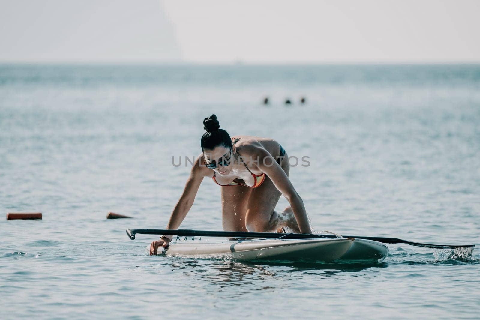 Sea woman sup. Silhouette of happy middle aged woman in rainbow bikini, surfing on SUP board, confident paddling through water surface. Idyllic sunset. Active lifestyle at sea or river