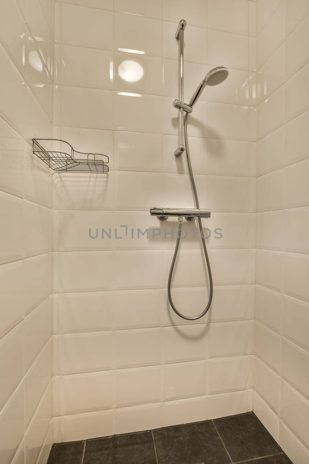 a shower with white tiles on the walls and black tile flooring in a small bathroom area that is very clean