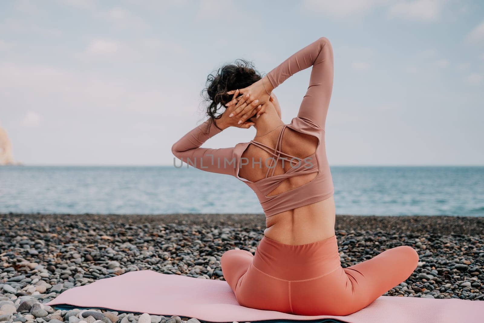 Middle aged well looking woman with black hair doing Pilates with the ring on the yoga mat near the sea on the pebble beach. Female fitness yoga concept. Healthy lifestyle, harmony and meditation.