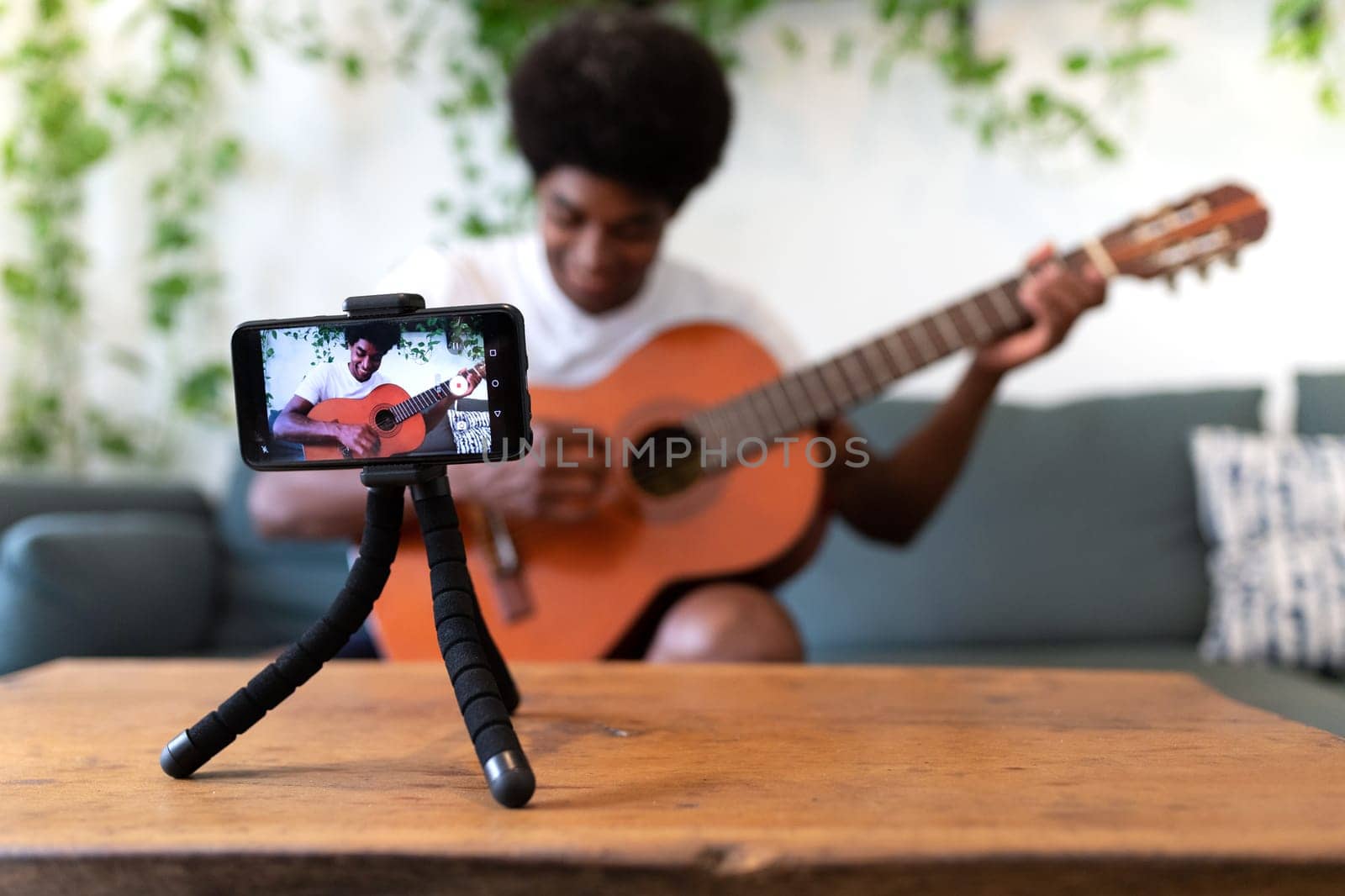 Young african american man recording a guitar lesson with his cellphone. Selective focus on phone. E-learning concept.