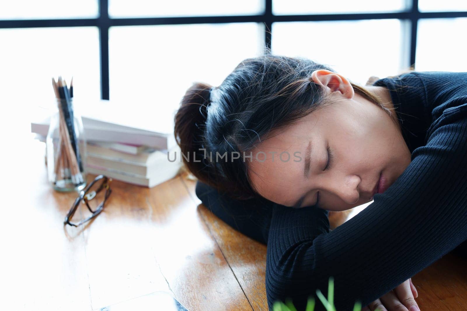 A portrait of a teenage Asian woman sleeping on a desk in the library due to fatigue from studying by Manastrong