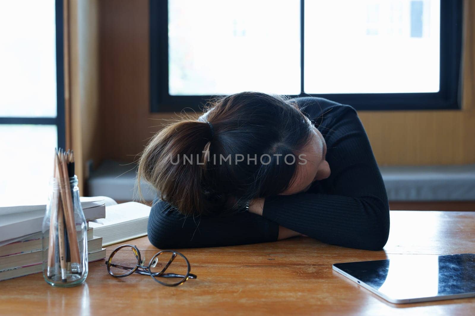 A portrait of a teenage Asian woman sleeping on a desk in the library due to fatigue from studying.