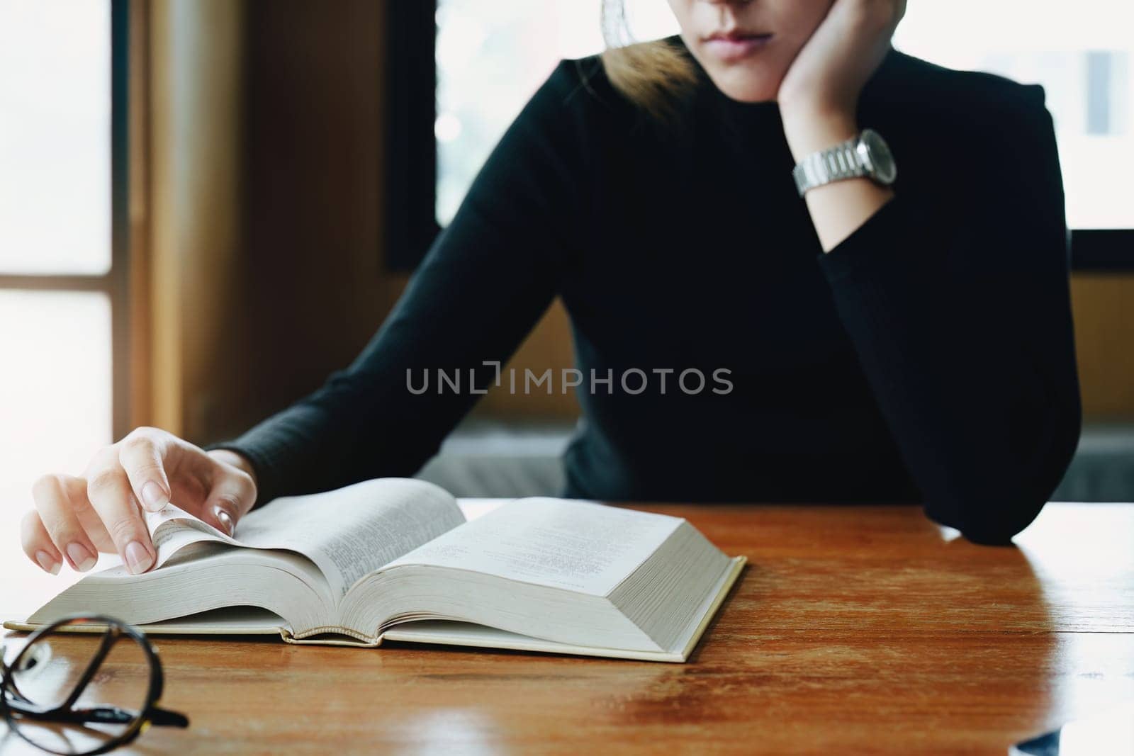 A portrait of a young Asian woman reading textbooks shows boredom on a wooden desk in library by Manastrong