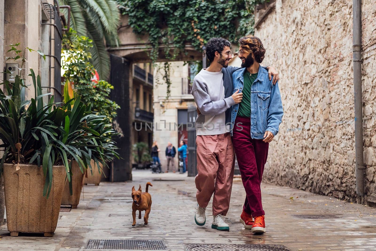 gay male couple walking with their dog along a beautiful cobbled street decorated with plants, concept of leisure and love between people of the same sex