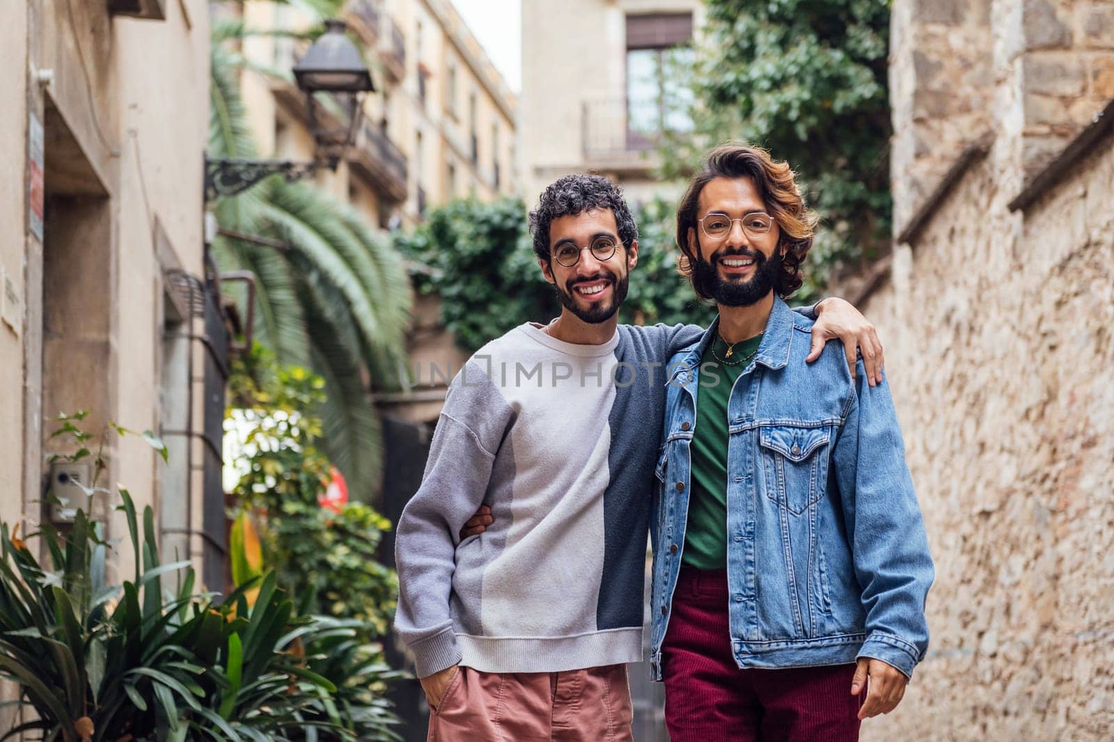 gay male couple embracing looking at camera smiling happy in a nice street with plants, concept of leisure and love between people of the same sex