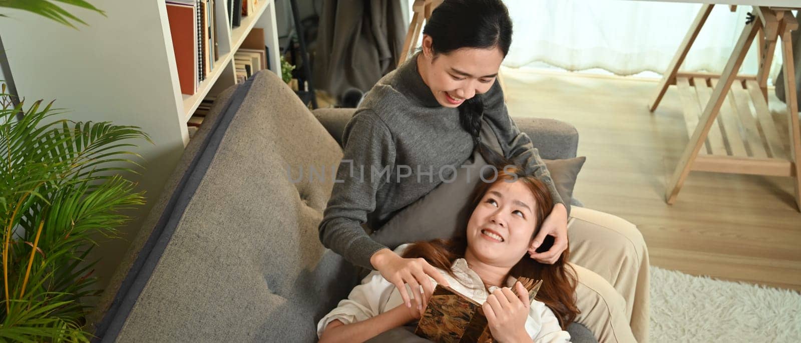 Happy young lesbian couple relaxing on couch, spending time together at home. Lgbt people lifestyle concept.