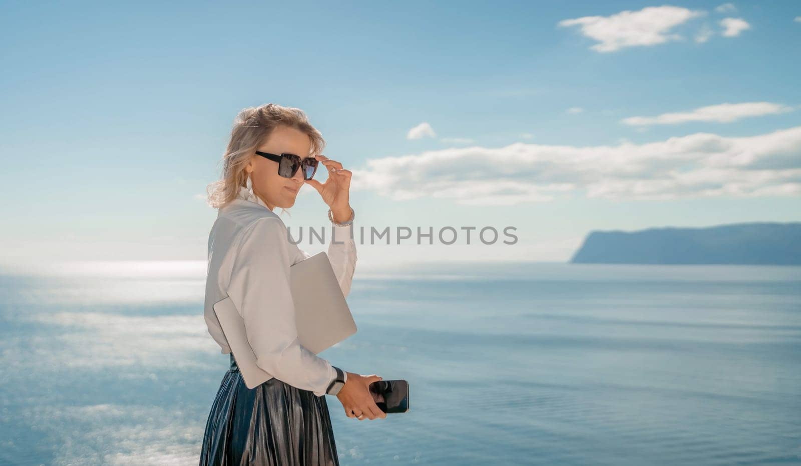 Freelance women sea working on a computer. Pretty middle aged woman with computer and phone outdoors with beautiful sea view. The concept of remote work