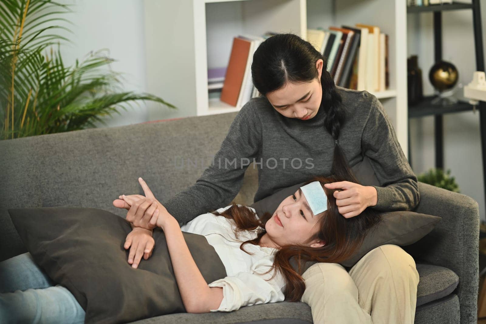 Affectionate women taking care of a sick girlfriend with fever on couch at home. LGBT, equal rights and love concept by prathanchorruangsak
