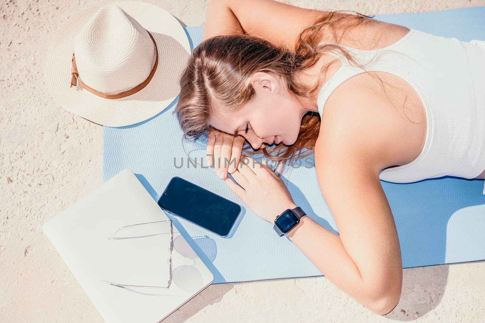 Successful business woman in yellow hat working on laptop by the sea. Pretty lady typing on computer at summer day outdoors. Freelance, travel and holidays concept.