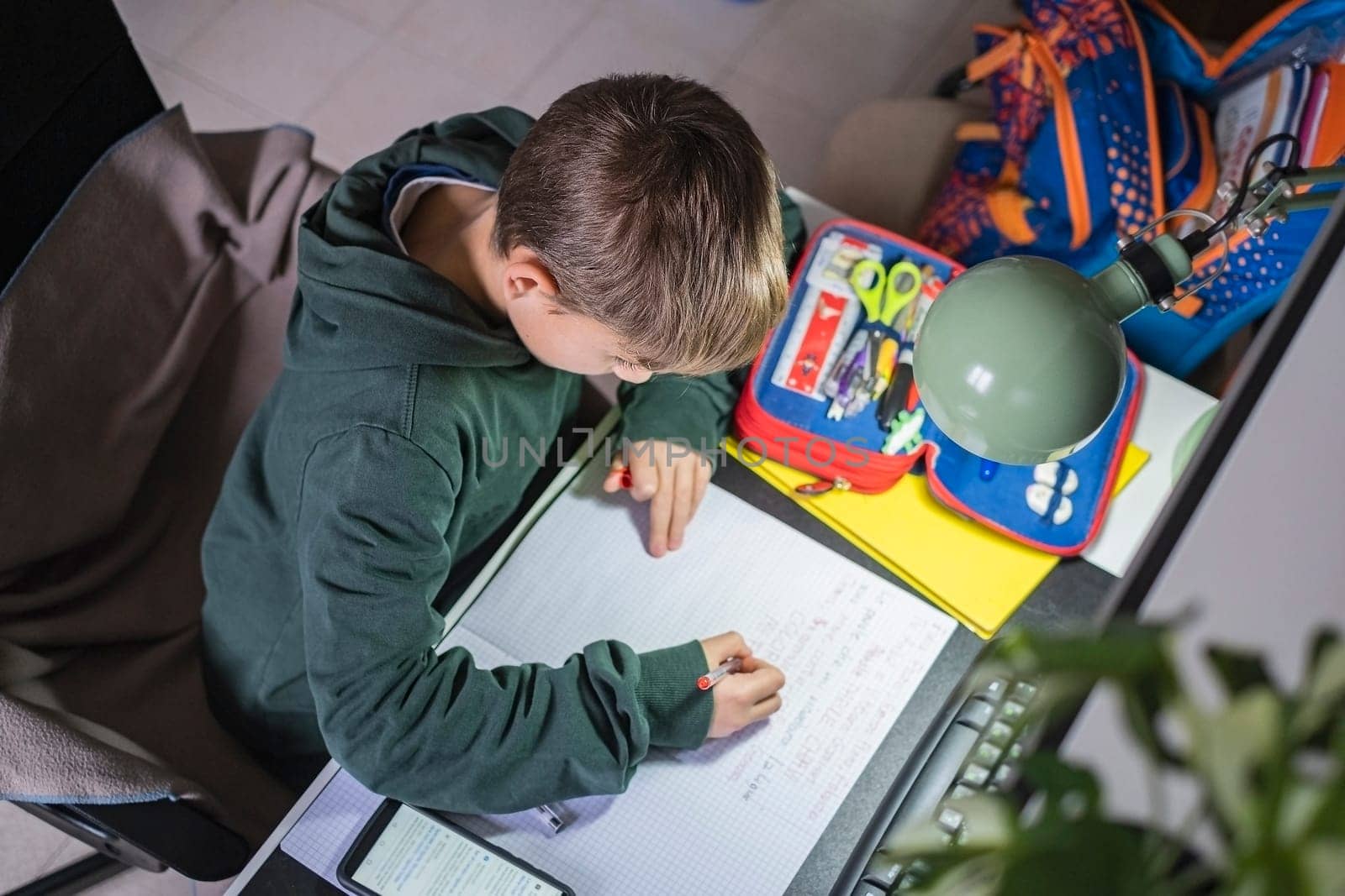 Top view of boy studying at home with book, writing and doing school homework.Distance learning online education. Back to school