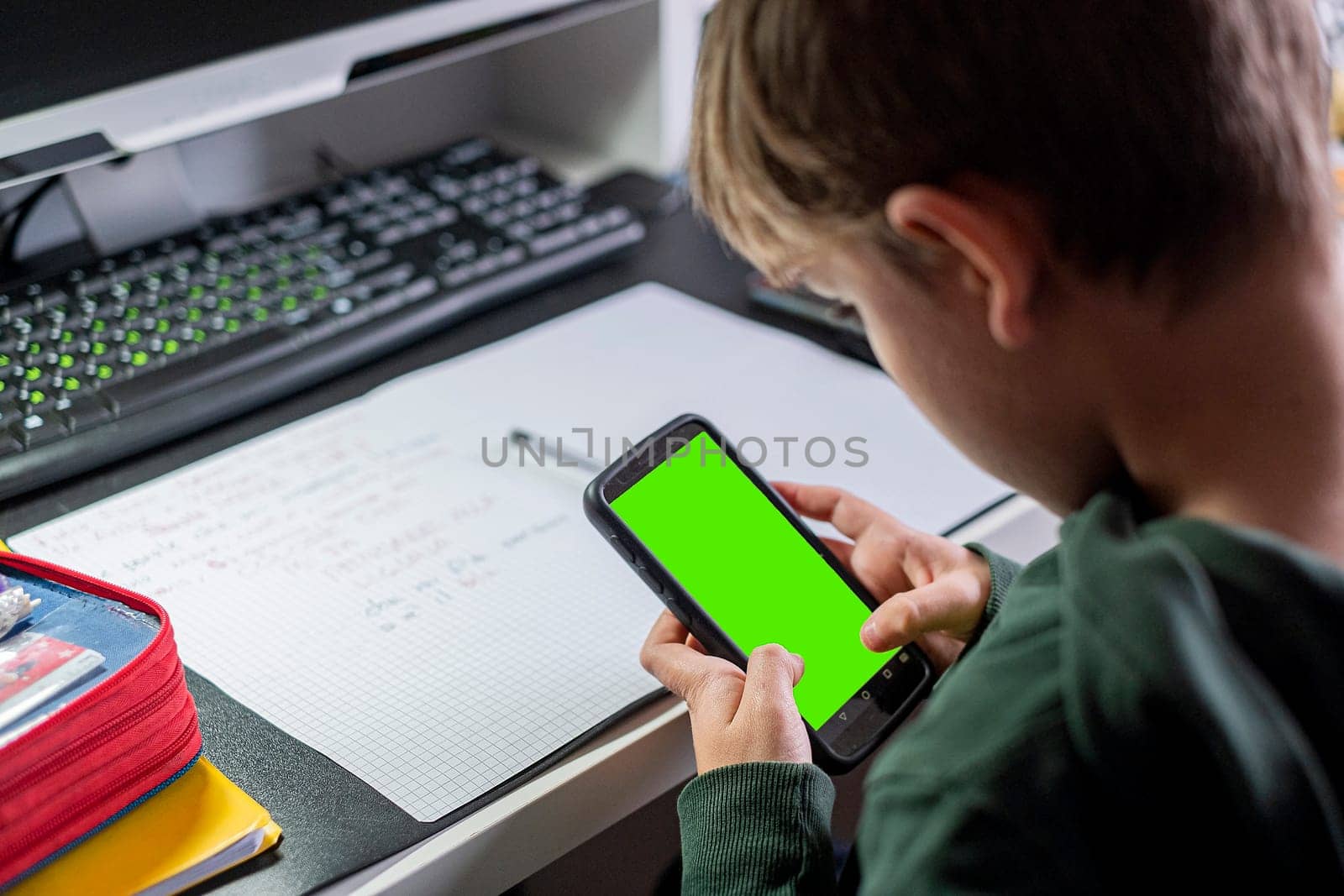 Kid boy studying at home with smartphone and doing school homework. Thinking caucasian child siting at table with mobile phone. Distance learning online education. Copy space.