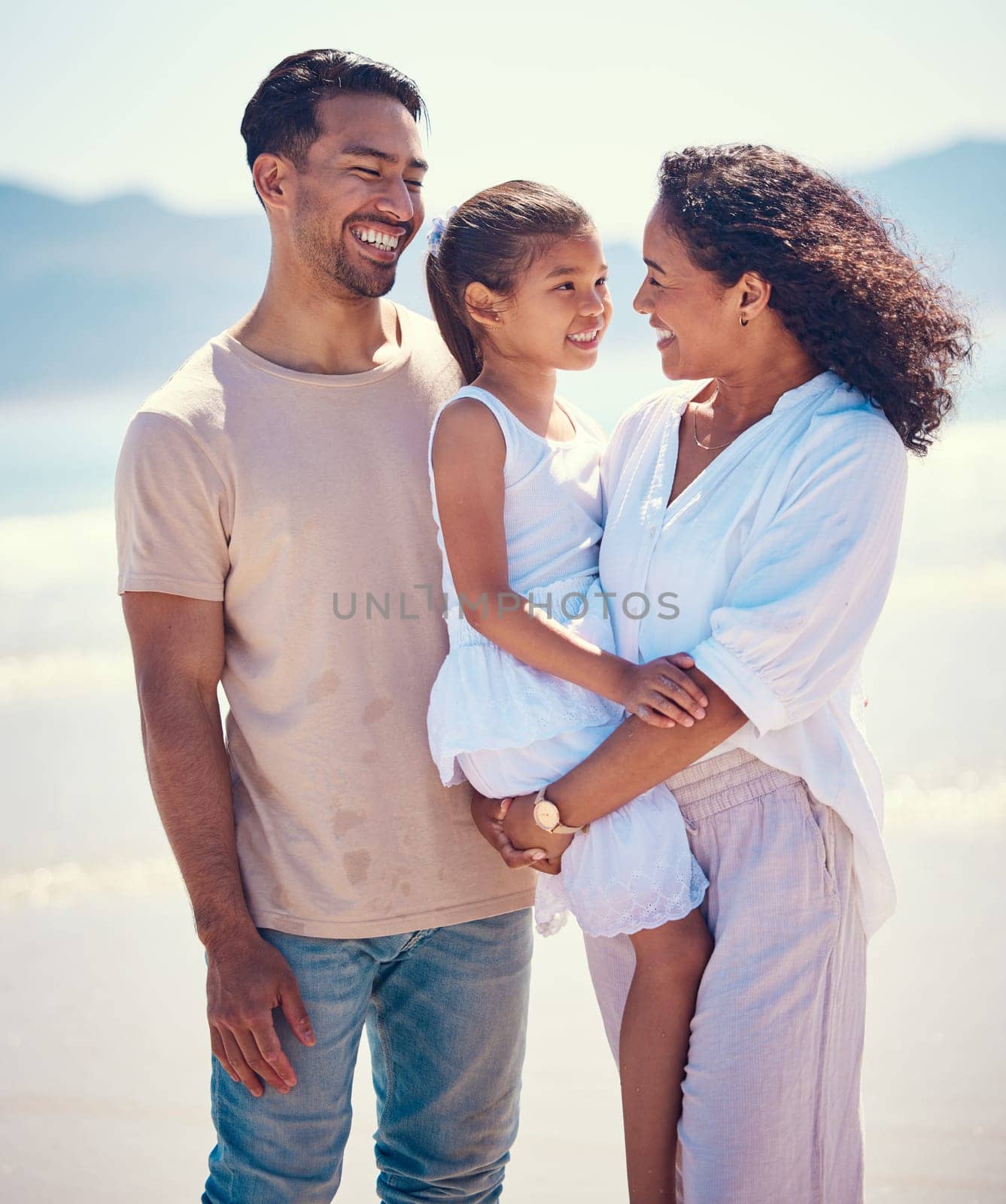 Happy family, beach and hug of a mother, father and girl together by the ocean. Nature, sea and love of a mom, dad and child from the Philippines on a vacation with parents on travel holiday.