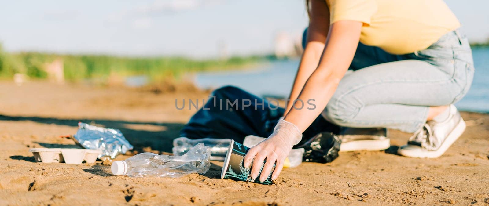 Young female volunteer hand satisfied with picking up trash, a plastic bottles and coffee cups, clean up beach with a sea. Woman collecting garbage. Environmental ecology pollution concept. Earth Day.