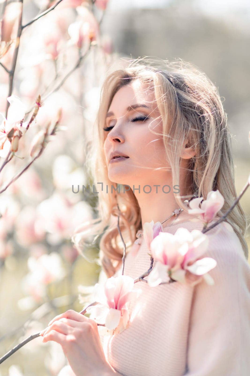 Portrait of a beautiful happy middle aged woman enjoying the smell in a blooming spring garden. Beautiful magnolia bushes, large flowers. by Matiunina