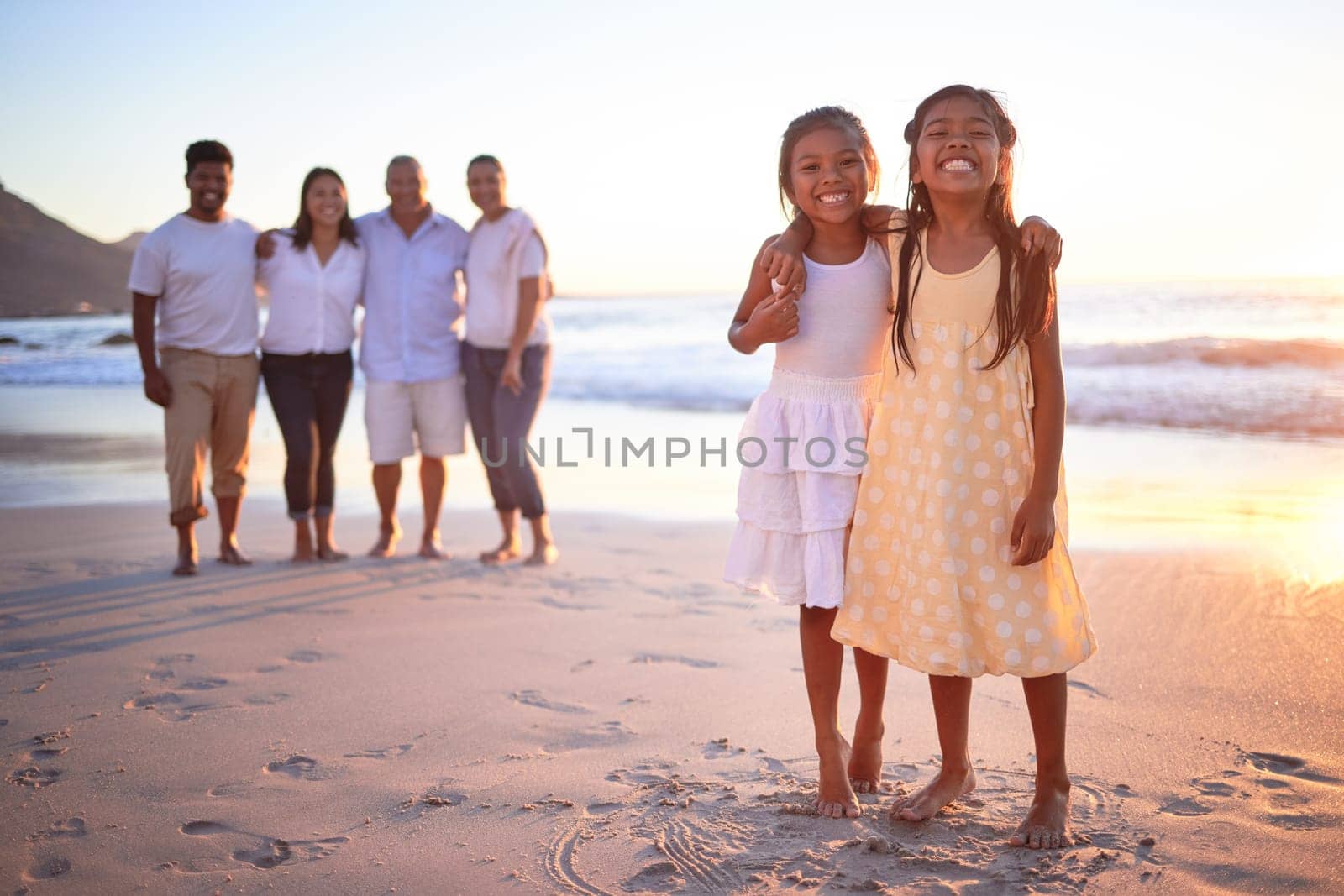 Children, beach and family with a girl and sister by the ocean or sea at sunset during summer vacation. Kids, love and travel with daughter siblings on holiday with their parents and grandparents by YuriArcurs