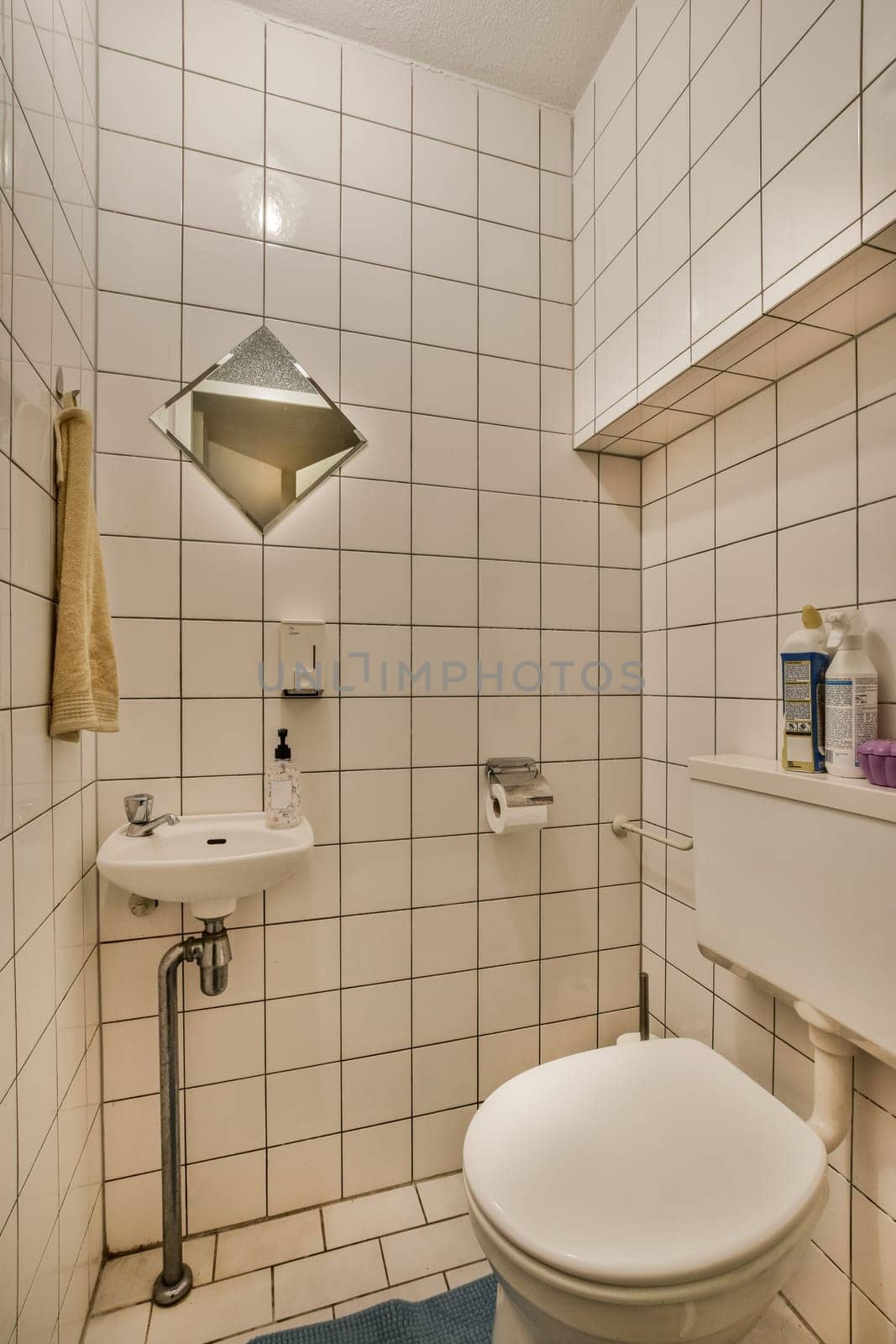 a bathroom with white tiles on the walls and blue rug in front of the toilet bowl, sink and mirror