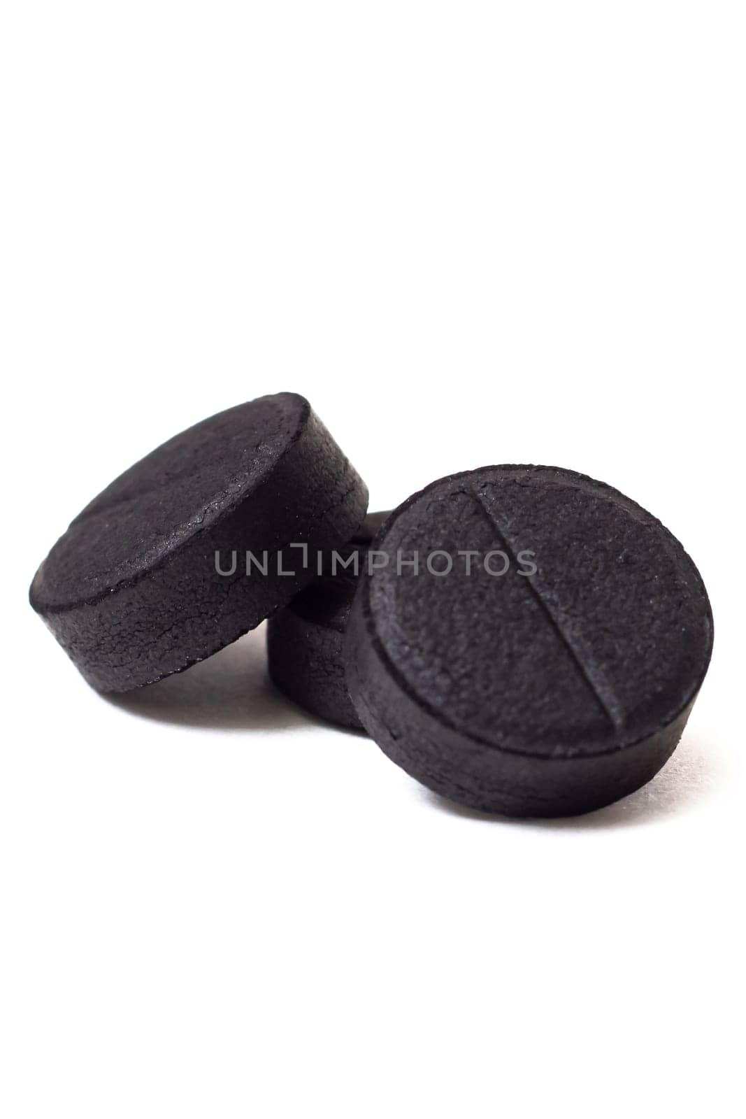 Three black charcoal tablets isolated on a white background close up