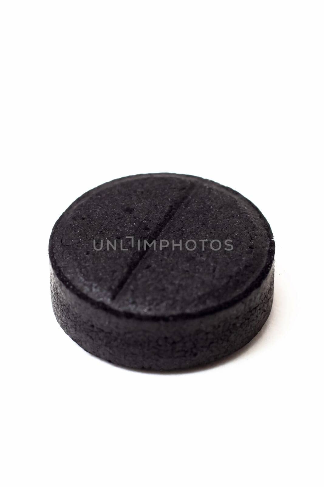 One black charcoal tablet isolated on a white background close up