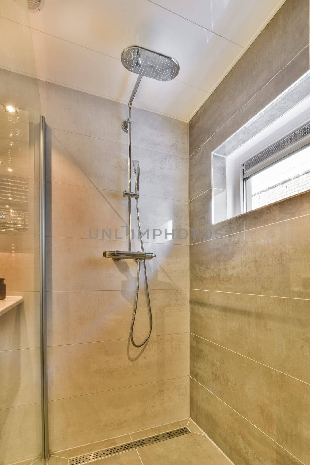 a shower room with tile flooring and beige colored tiles on the walls there is a window in the background