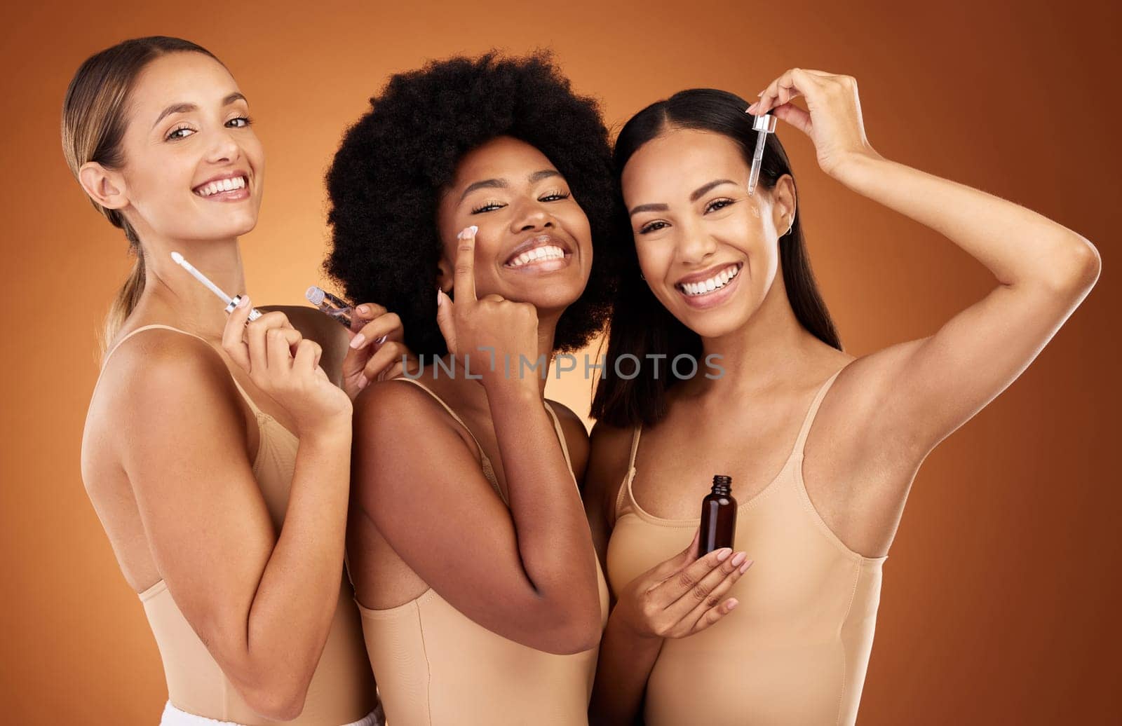 Diversity, women and with makeup lotion for cosmetics, natural beauty and skincare with brown studio background. Portrait, girls and smile with eyecare, cream and oils for wellness, happy or collagen by YuriArcurs