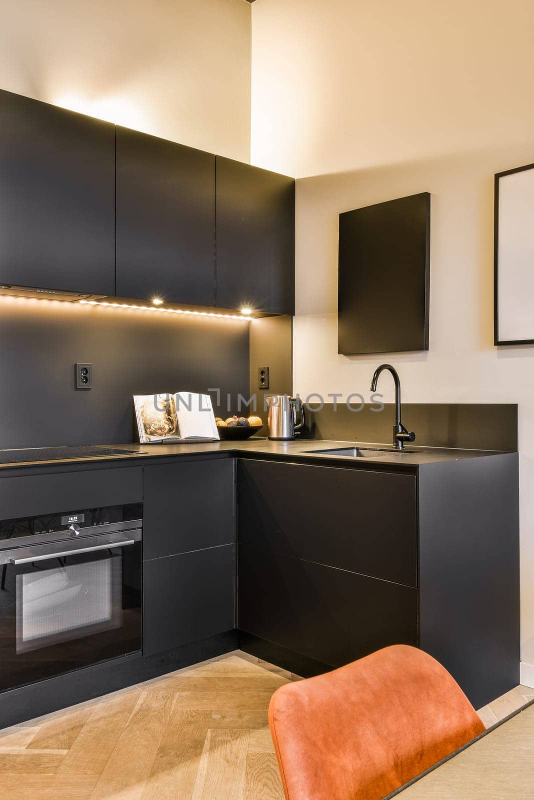Amsterdam, Netherlands - 10 April, 2021: a modern kitchen with black cabinets and an orange chair in the center of the photo is framed on the wall