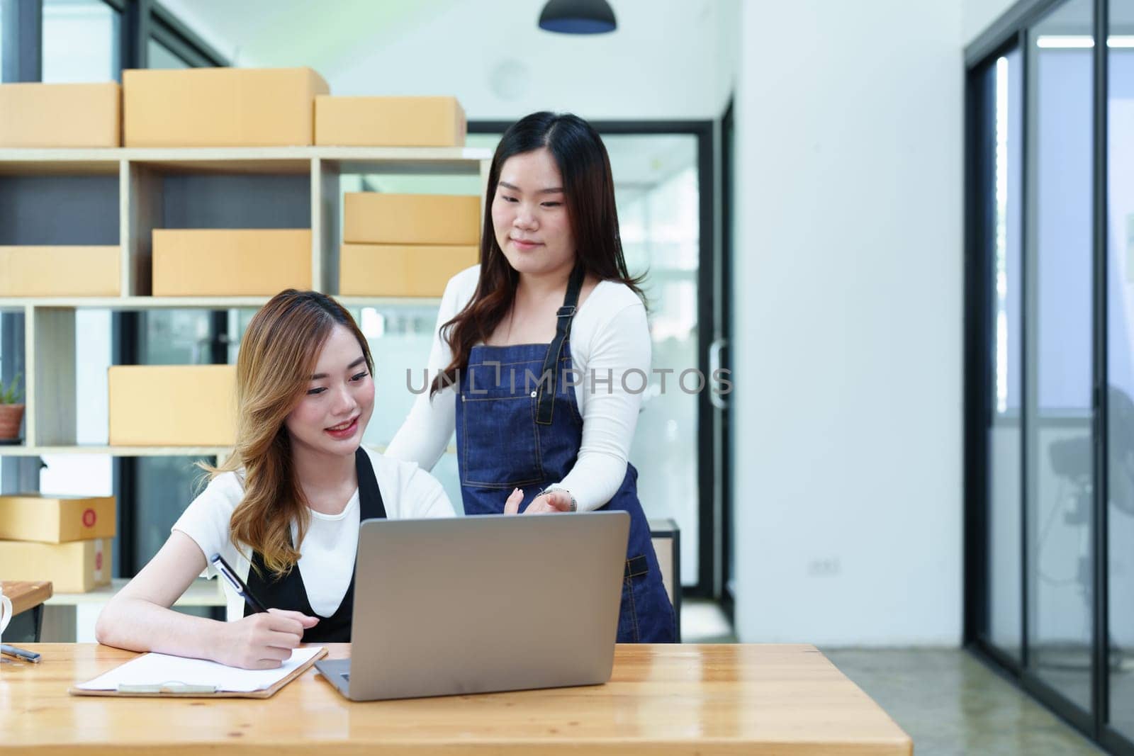 Starting small business entrepreneur of independent Asian woman smiling using computer laptop with cheerful success of online marketing package box items and SME delivery concept by Manastrong