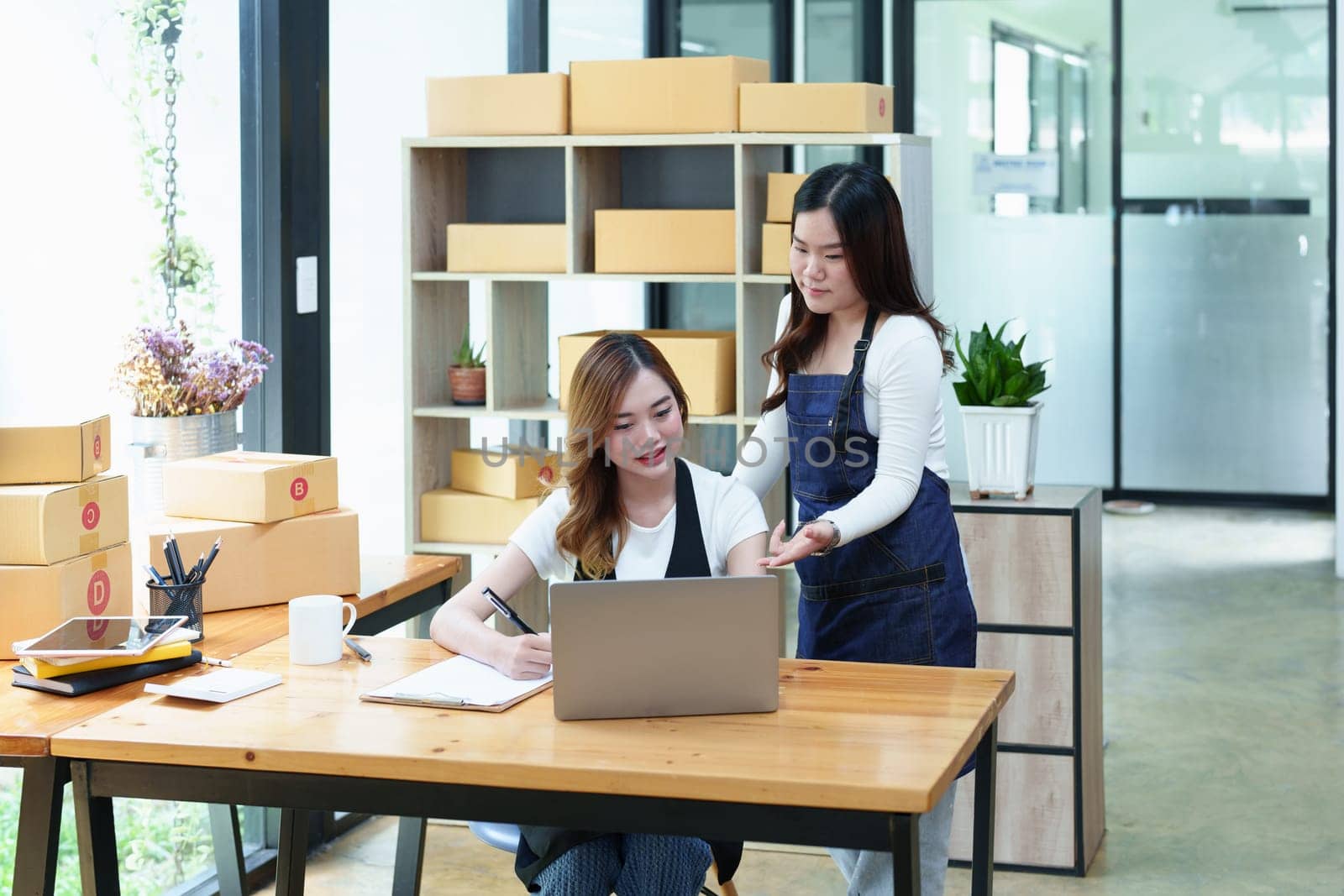 Starting small business two entrepreneur of independent Asian woman smiling using computer laptop with cheerful success of online marketing package box items and SME delivery concept by Manastrong