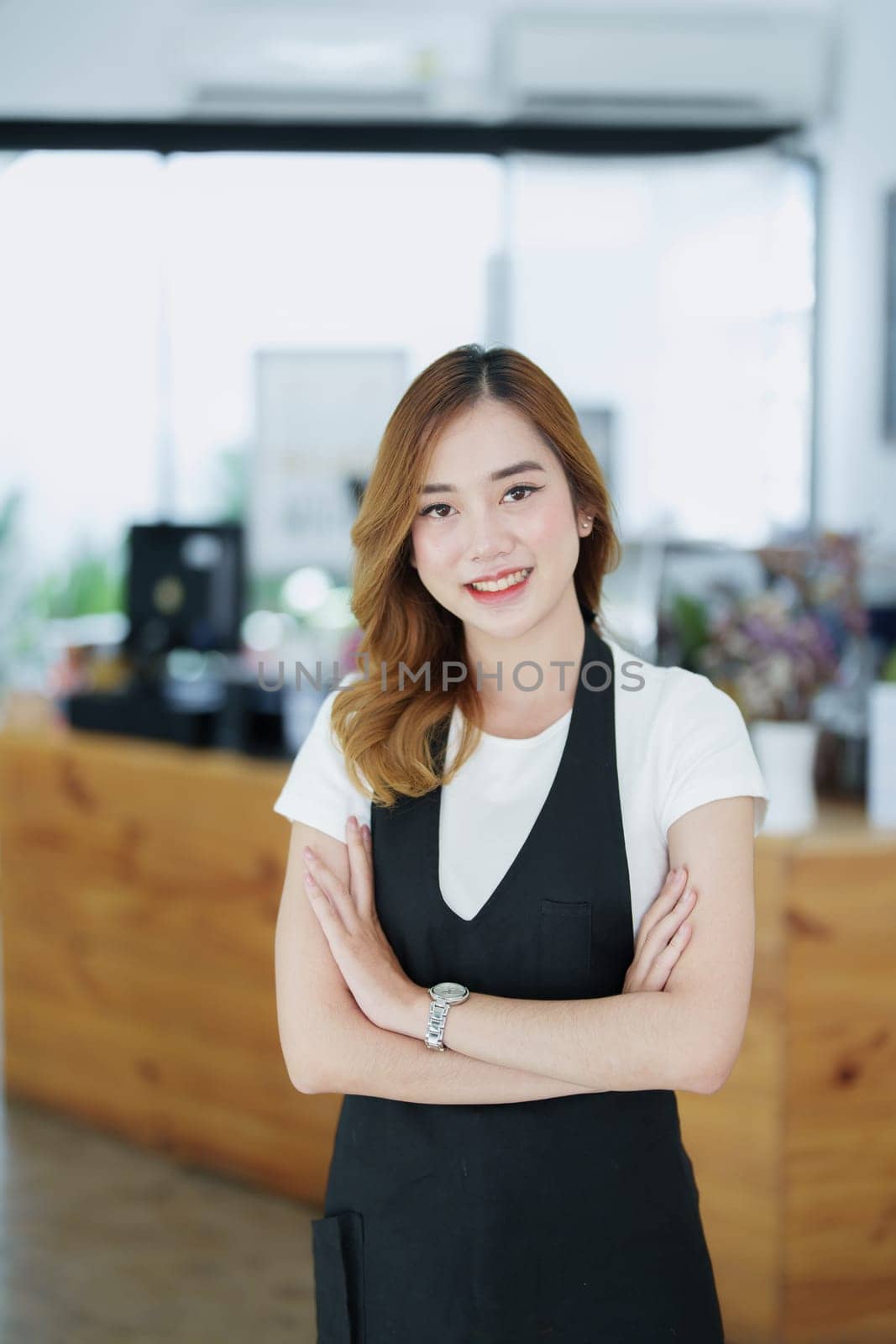 Starting and opening a small business, a young Asian woman showing a smiling face in an apron standing in front of a coffee shop bar counter. Business Owner, Restaurant, Barista, Cafe, Online SME by Manastrong