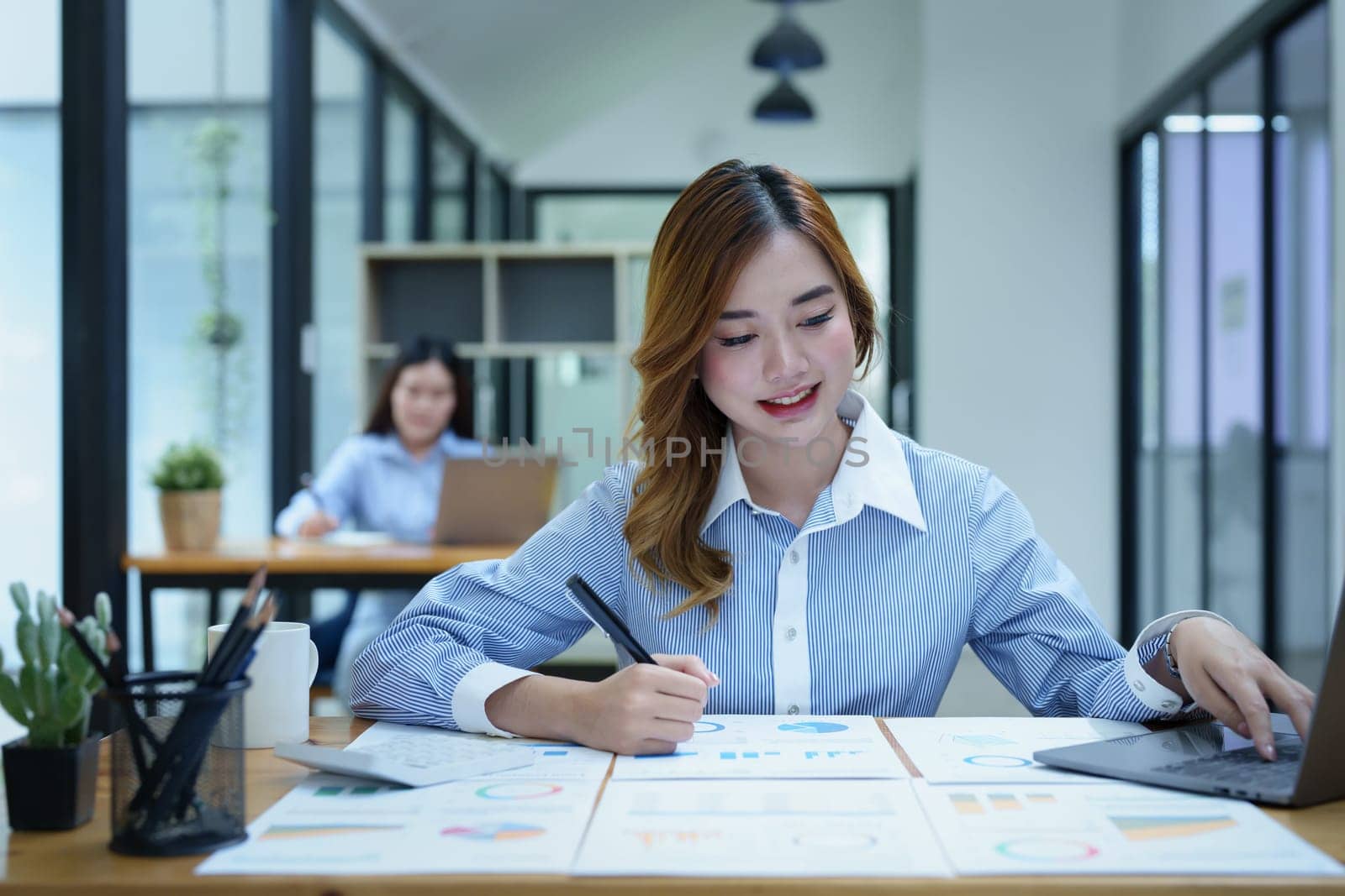 Portrait of a thoughtful Asian businesswoman looking at financial statements and making marketing plans using a computer on her desk.