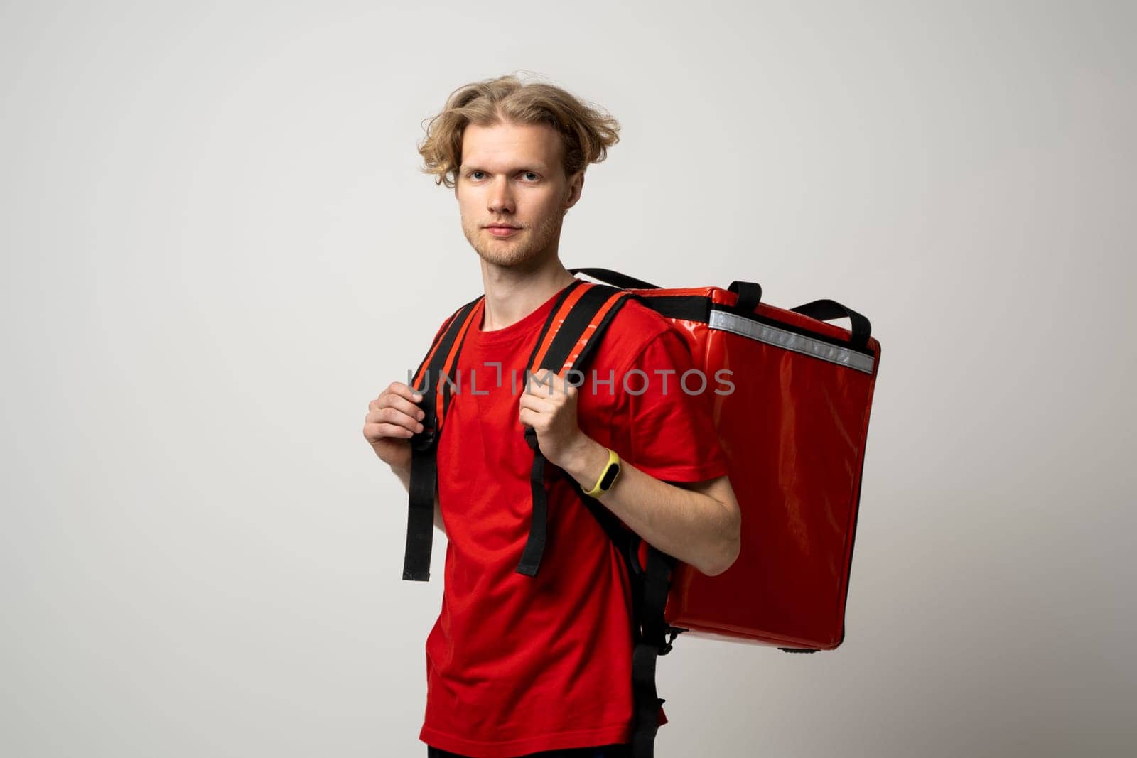 Delivery man in red uniform with thermal backpack for food. Takeaway food delivery. Man delivering online food orders to customers with red thermal bag, grocery deliver. by vovsht