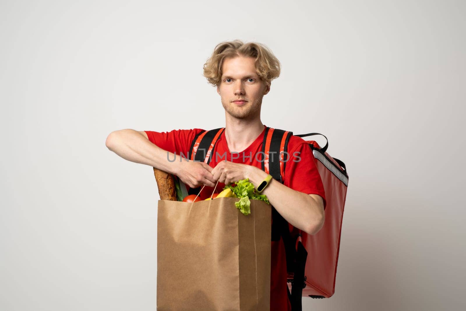 Portrait of smiling cheerful handsome young delivery man holding grocery shopping bag isolated on white background