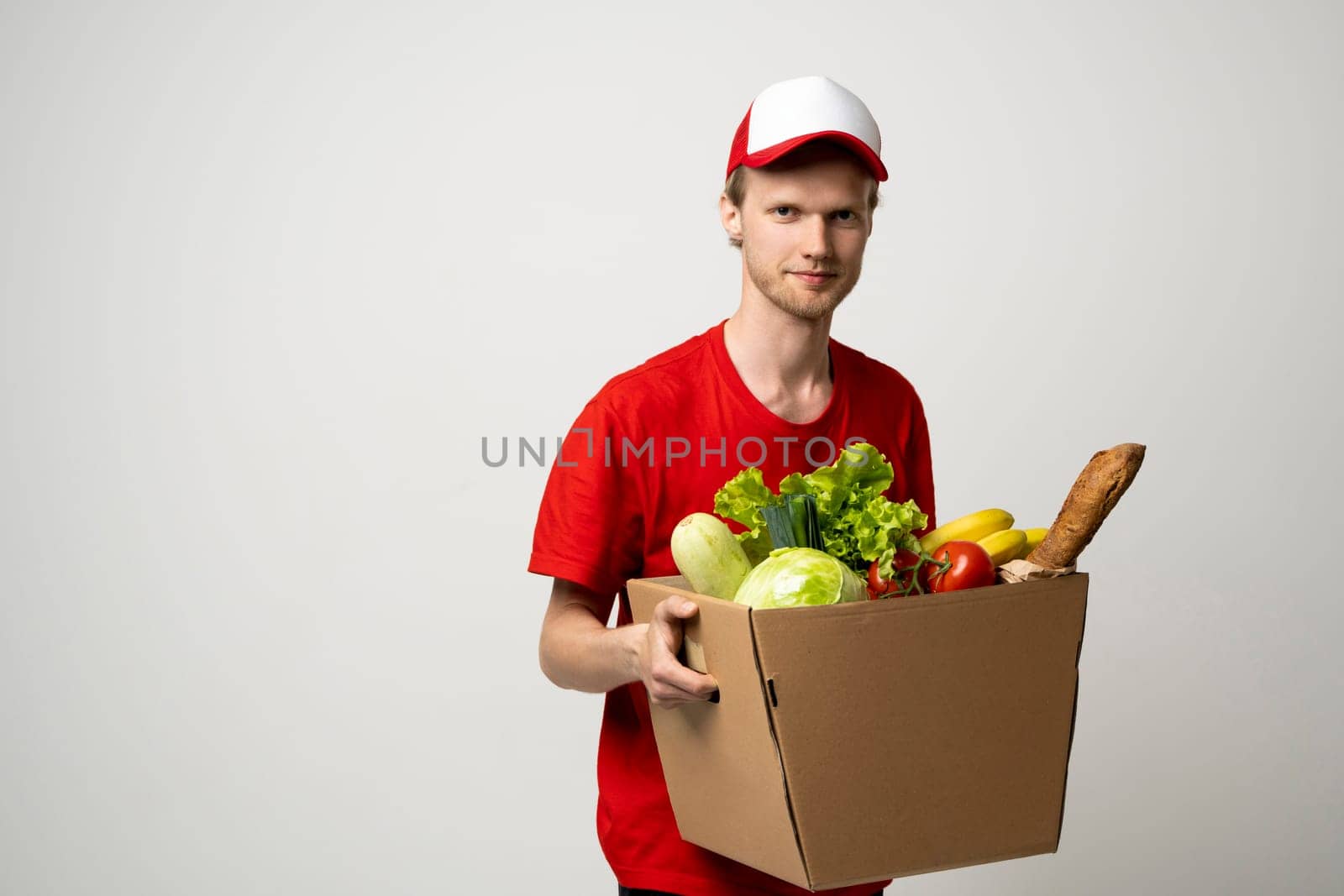 Delivery man in a red uniform holding paper box with a groceries. Fast and free delivery transport . Online shopping and express delivery