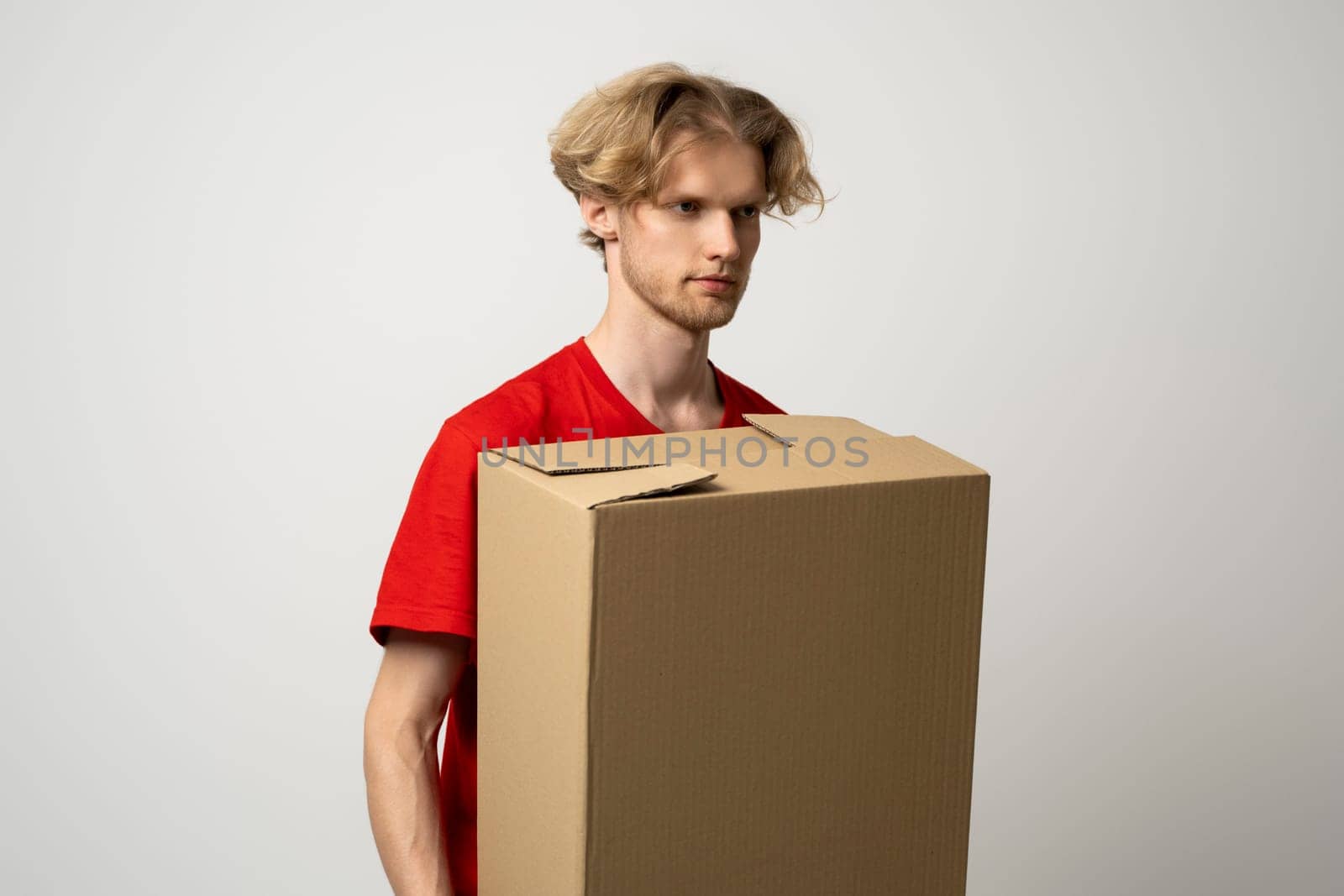 Delivery service. Happy young delivery man in red t-shirt standing with parcel isolated on white background. by vovsht