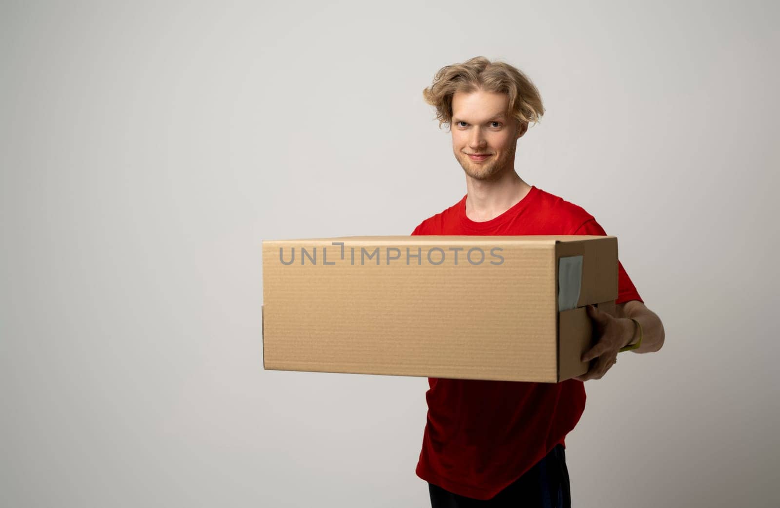 Smiling delivery man in red uniform giving cardbox on white background